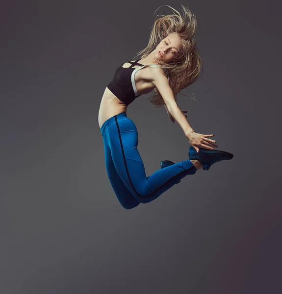 スポーツ ウエアで若いバレリーナの踊りし、スタジオでジャンプします。灰色の背景に分離. — ストック写真