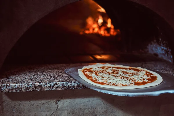 Chef zet pizza in de oven voor het bakken — Stockfoto