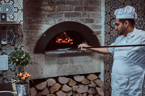 Italian chef is putting gourmet freshly made pizza to the stone oven.