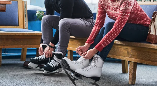 Молодая пара сидит на скамейке и завязывает шнурки хоккейных коньков в раздевалке — стоковое фото