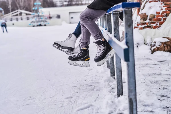 Couple wearing ice skates sitting on a guardrail