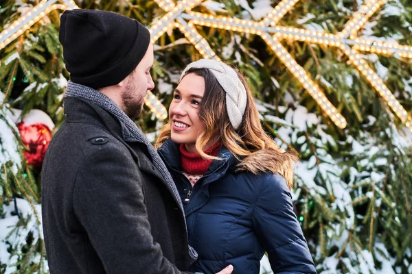 따뜻 한 옷을 입은 젊은 부부가 손을 잡고 도시 크리스마스 트리 근처에서 서 서로를바라보며 함께 시간을 보내고 있다. — 스톡 사진
