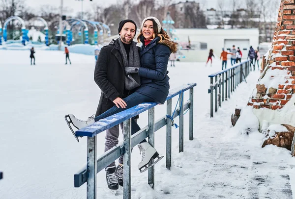 Verliebtes Paar, Date auf der Eisbahn, ein Mädchen sitzt auf einer Leitplanke und umarmt ihren Freund. — Stockfoto