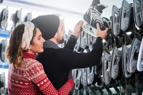 Junges Paar steht mit vielen Paar Schlittschuhen in der Nähe der Ablage und wählt seine Größe — Stockfoto