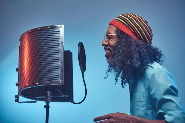 Afrikaanse Rastafari zanger man draagt een blauw shirt en beanie emotioneel schrijven lied in de opnamestudio. — Stockfoto