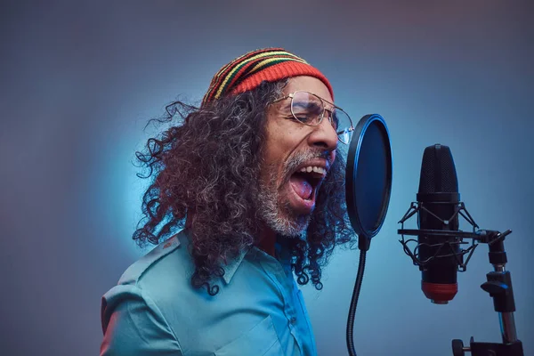 Αφρικανός Rastafarian τραγουδιστής άντρας φορώντας ένα μπλε πουκάμισο και beanie τραγούδι συναισθηματικής γραφής στο στούντιο ηχογράφησης. — Φωτογραφία Αρχείου