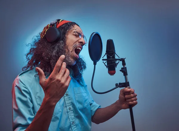 Afrikanischer rastafarischer Sänger in blauem Hemd und Mütze, der im Tonstudio emotional Songs schreibt. — Stockfoto