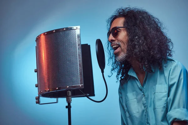 African vocal artist wearing a blue shirt emotionally writing song in the recording studio.