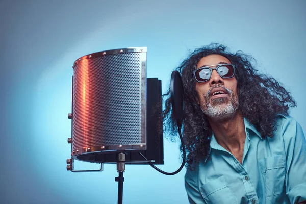 African vocal artist wearing a blue shirt emotionally writing song in the recording studio.