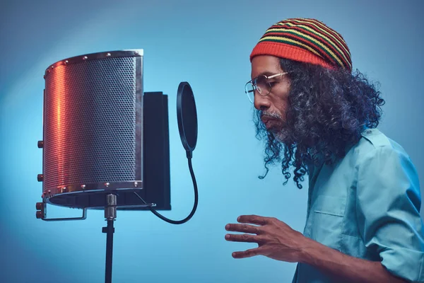 Afrikansk Rastafarian sångerska man bär en blå skjorta och mössa känslomässigt skriva låt i inspelningsstudion. — Stockfoto