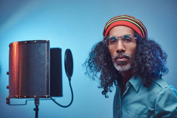 Afrikanischer rastafarischer Sänger in blauem Hemd und Mütze, der im Tonstudio emotional Songs schreibt. — Stockfoto