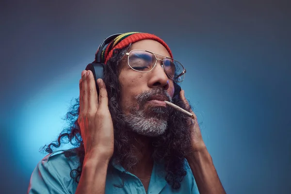 Studio πορτρέτο της Αφρικής Rastafarian αρσενικό απολαμβάνει τη μουσική στα ακουστικά και το κάπνισμα ζιζανίων. — Φωτογραφία Αρχείου