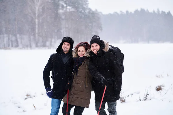 Amigos caminham no frio floresta nevada ficar em um abraço e olhar para a câmera . — Fotografia de Stock