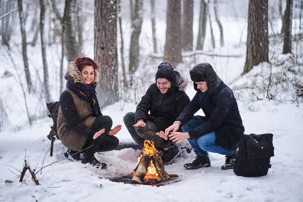 Vrienden van reizigers koesteren zich in een vuur in het besneeuwde bos — Stockfoto