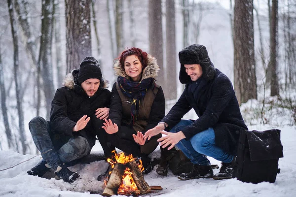 Amigos de viajantes se aquecem em um incêndio na floresta nevada — Fotografia de Stock