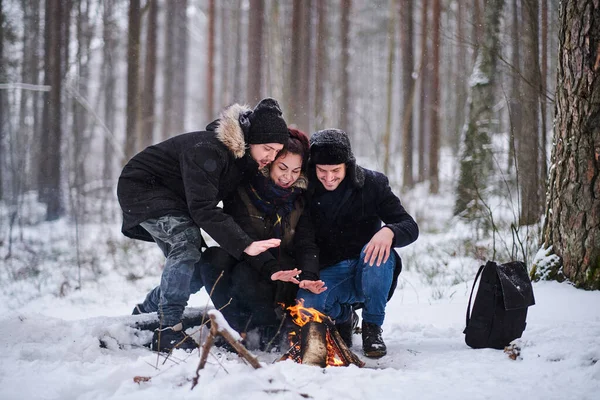 Amigos de viajantes se aquecem em um incêndio na floresta nevada — Fotografia de Stock