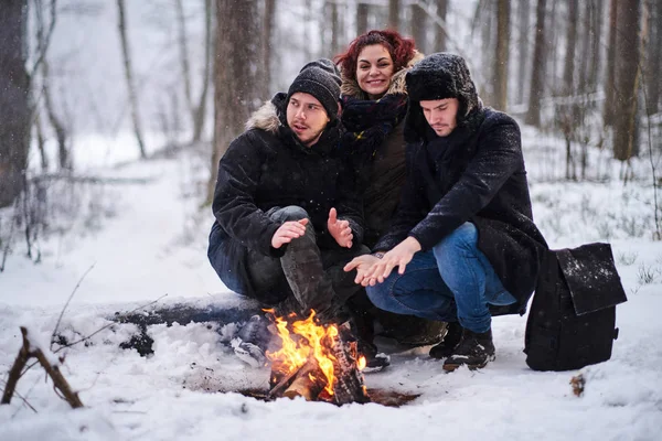 Freunde von Reisenden sonnen sich in einem Feuer im verschneiten Wald — Stockfoto