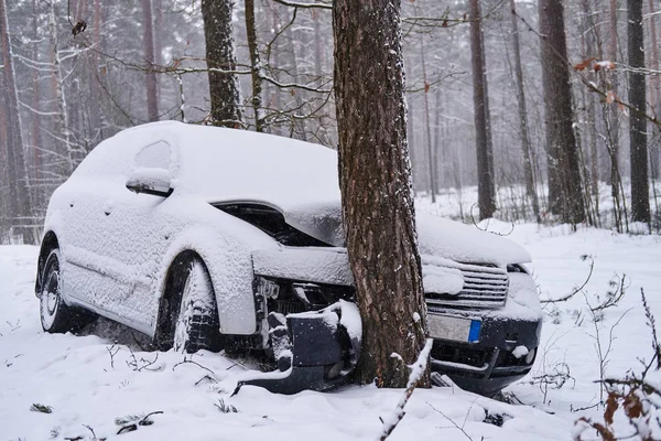 Une voiture cassée s'écrase dans un arbre après avoir perdu le contrôle sur une route glissante dans une forêt enneigée . — Photo