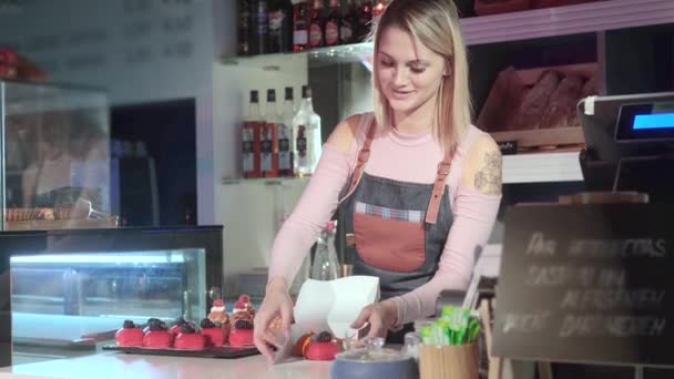 Όμορφη νεαρή κοπέλα πωλητής συσκευάζει κέικ στέκεται στον πάγκο στο ζαχαροπλαστείο — Αρχείο Βίντεο