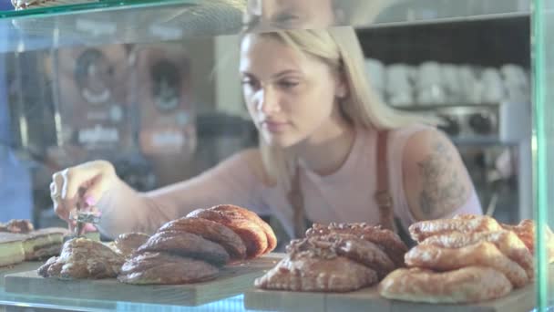 Linda jovem vendedora que trabalha na confeitaria. Close-up de doces frescos em um vitrine — Vídeo de Stock