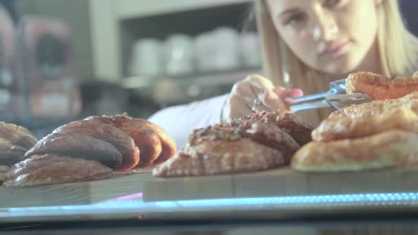 Beautiful young female seller working in the confectionery store. Close-up of fresh pastries on a vitrine — ストック動画