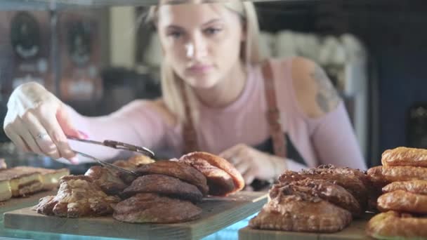 Hermosa joven vendedora que trabaja en la confitería. El primer plano de la cocción fresca sobre la vitrina — Vídeos de Stock