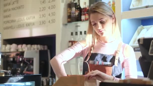 Красивая юная продавщица упаковывает торты, стоящие у стойки в кондитерском магазине. — стоковое видео
