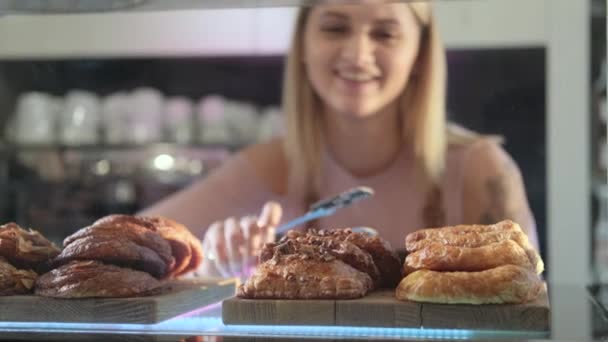 Beautiful young female seller working in the confectionery store. Close-up of fresh pastries on a vitrine — Stock Video