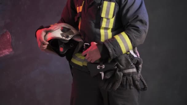 Zbliżenie widok dzielnego strażaka w specjalnym mundurze trzyma kask ochronny stojący pod szarą ścianą — Wideo stockowe