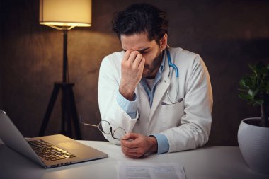 Yorgun doktor masanın yanında oturuyor.