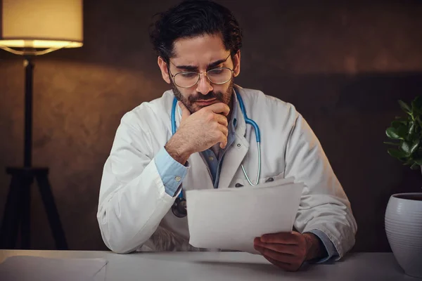 Занятый доктор в своем кабинете работает с бумагами — стоковое фото
