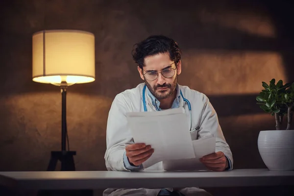 O médico ocupado no escritório dele está a trabalhar com papeladas. — Fotografia de Stock