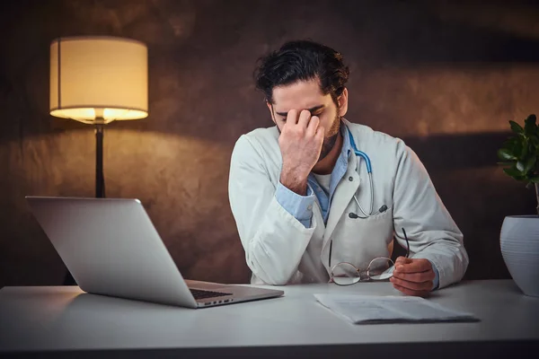 Médico cansado está sentado ao lado da mesa — Fotografia de Stock