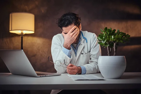 Médico cansado está sentado ao lado da mesa — Fotografia de Stock