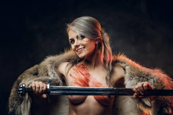 Szexi fantázia harcos nő, meztelen törzzsel, bundában és karddal a kezében, őrült tekintettel néz a kamerába. Cosplayer mint Ciri a Boszorkányból — Stock Fotó