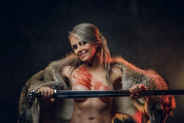 Sexy fantasy warrior woman with naked torso wearing fur and holding sword, looking on a camera with crazy look. Cosplayer as Ciri from The Witcher — Stock Photo, Image