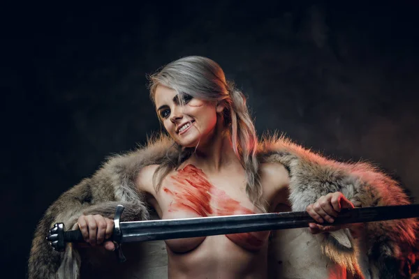 Sexy fantasy warrior woman with naked torso wearing fur and holding sword, looking on a camera with crazy look. Cosplayer as Ciri from The Witcher