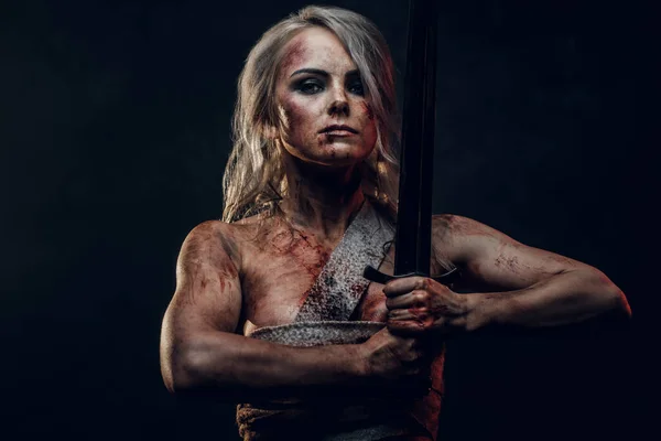 Mulher nua guerreira vestindo pano de pano manchado com sangue e lama posando com uma espada. Foto de estúdio sobre um fundo escuro. Cosplayer como Ciri de The Witcher — Fotografia de Stock