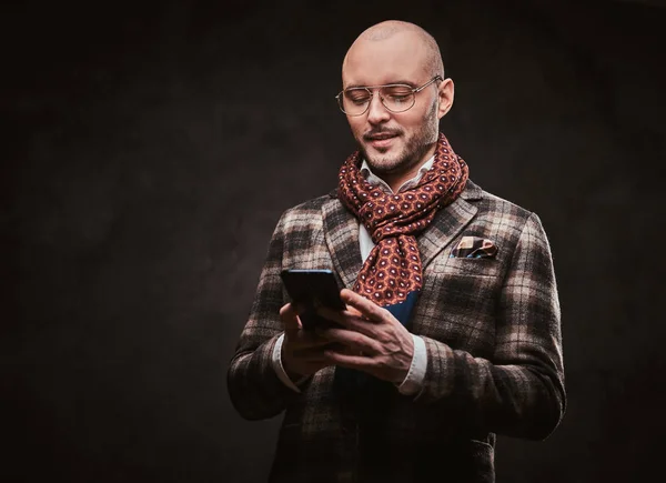 Empresário elegante bem sucedido posando em um estúdio usando jaqueta quadriculada, óculos e cachecol enquanto segura um smartphone — Fotografia de Stock