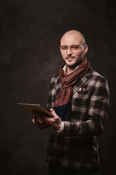 Empresário elegante bem sucedido posando em um estúdio usando jaqueta quadriculada, óculos e cachecol enquanto segura um tablet — Fotografia de Stock