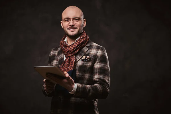 Exitoso hombre de negocios elegante posando en un estudio con chaqueta a cuadros, gafas y bufanda mientras sostiene una tableta —  Fotos de Stock