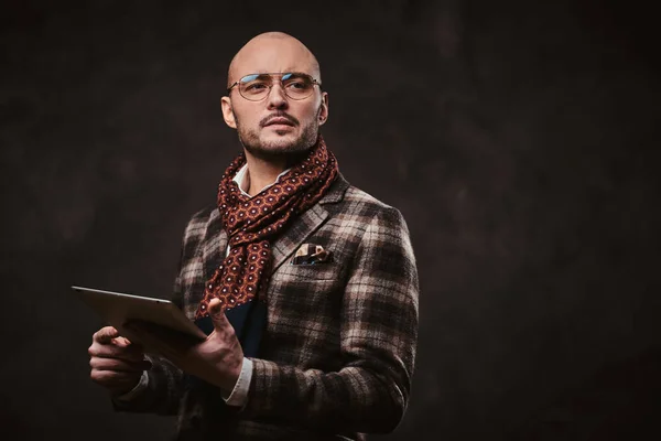 Erfolgreicher Geschäftsmann posiert in karierter Jacke, Brille und Schal im Studio und hält ein Tablet in der Hand — Stockfoto