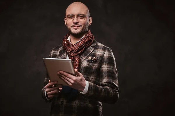 Erfolgreicher Geschäftsmann posiert in karierter Jacke, Brille und Schal im Studio und hält ein Tablet in der Hand — Stockfoto