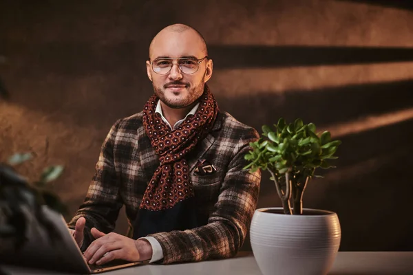 Bald europeu bem vestido sorridente empresário sentado no escritório em uma mesa com notebook, vestindo jaqueta elegante e um lenço — Fotografia de Stock