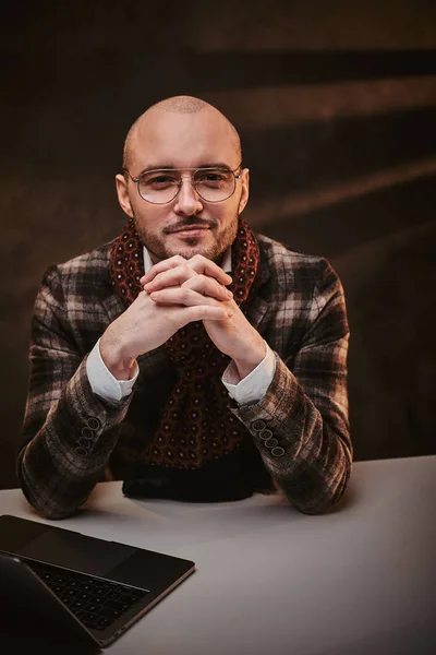 Bald europeu bem vestido sorridente empresário sentado no escritório em uma mesa com notebook, vestindo jaqueta elegante e um lenço — Fotografia de Stock