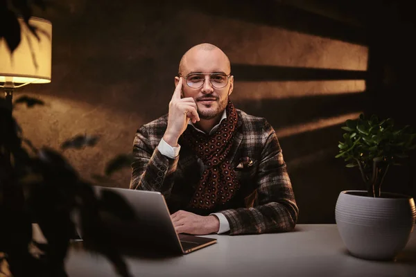 Calvo europeo bien vestido hombre de negocios cansado sentado en la oficina en una mesa con cuaderno, con una chaqueta elegante y una bufanda —  Fotos de Stock