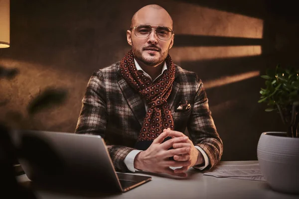 Glatzköpfiger, seriöser Geschäftsmann sitzt im Büro an einem Tisch mit Notizbuch, trägt schicke Jacke und Schal — Stockfoto