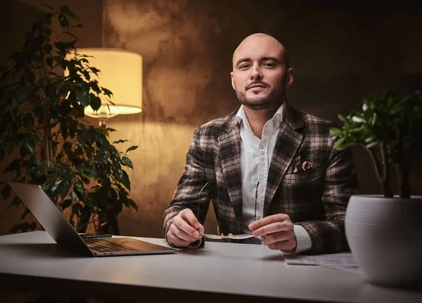 Καραφλός Ευρωπαίος καλοντυμένος επιχειρηματίας κάθεται στο γραφείο σε ένα τραπέζι με σημειωματάριο, φορώντας κομψό σακάκι — Φωτογραφία Αρχείου