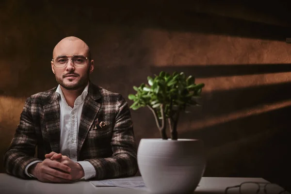 Καραφλός Ευρωπαίος καλοντυμένος επιχειρηματίας που κάθεται στο γραφείο σε ένα τραπέζι με σημειωματάριο, φορώντας κομψό σακάκι και γυαλιά — Φωτογραφία Αρχείου