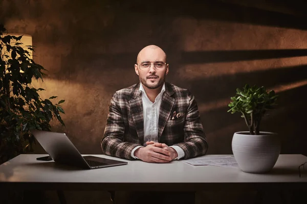 Bald europeu bem vestido interessado empresário sentado no escritório em uma mesa com notebook, vestindo jaqueta elegante — Fotografia de Stock